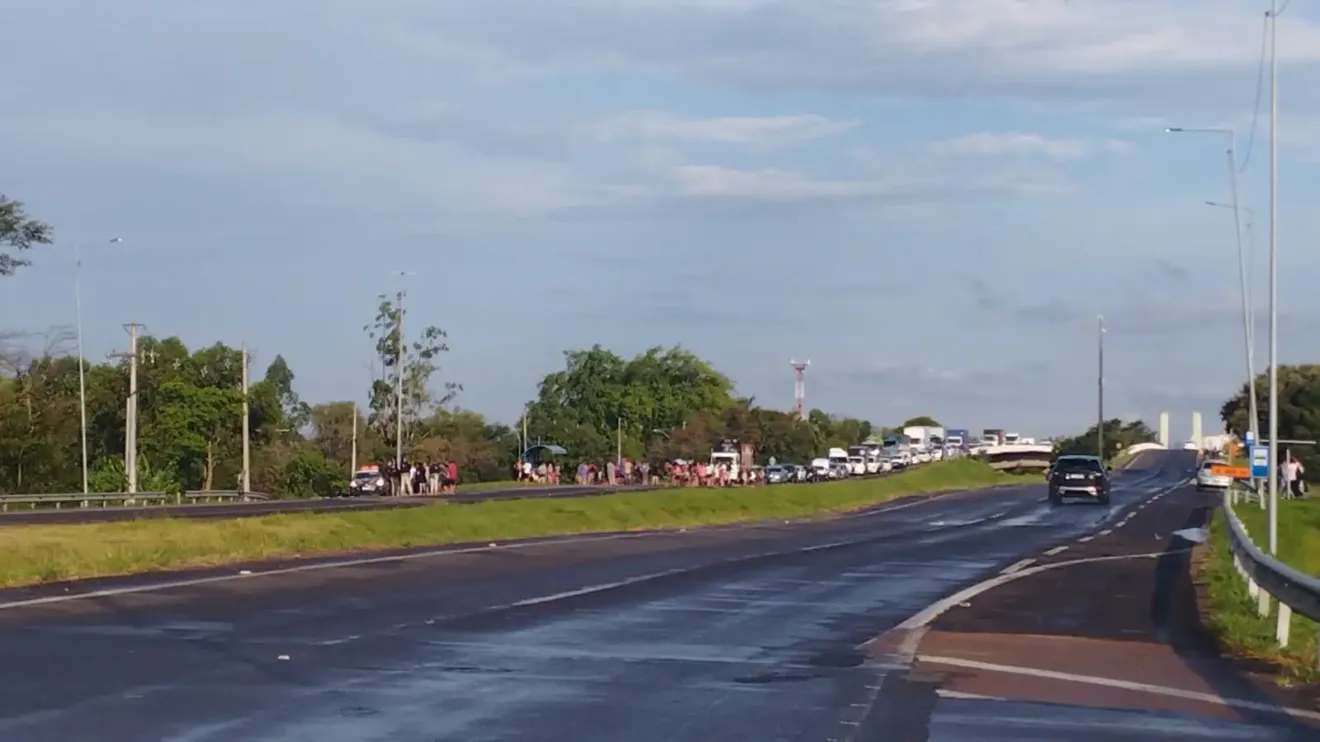 Protesto bloqueia BR-290, causando congestionamento. Várias pessoas e veículos na estrada demonstram insatisfação.