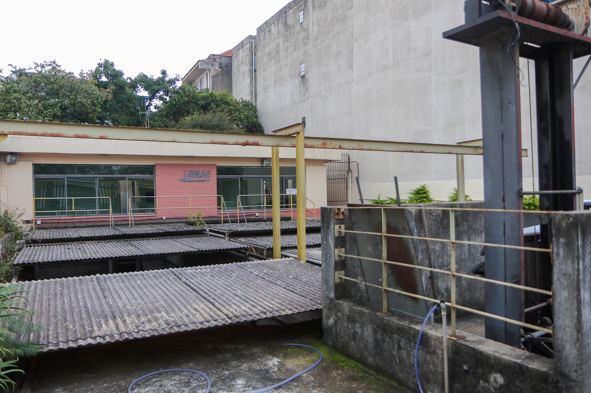 Imagem de um espaço urbano com estruturas de estacionamento e uma edificação ao fundo. O local é cercado por vegetação, apresentando uma atmosfera de tranquilidade em meio à cidade.