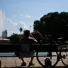 Pessoa relaxando em um banco de parque, com uma fonte ao fundo e uma bicicleta ao lado, aproveitando um dia ensolarado em Porto Alegre