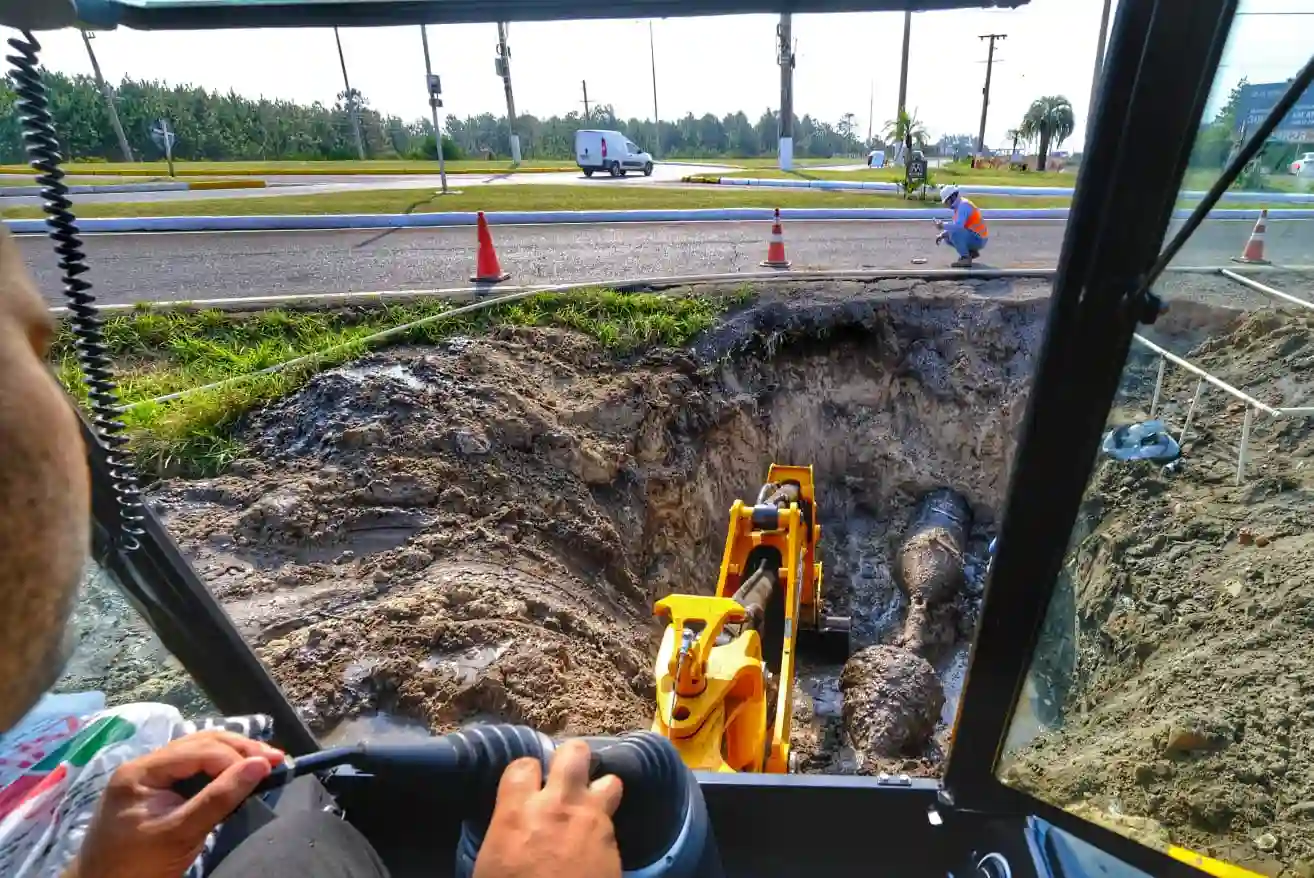 Imagem mostrando a operação de escavação com maquinário pesado, focando na profundidade da vala e no motorista na cabine do equipamento.