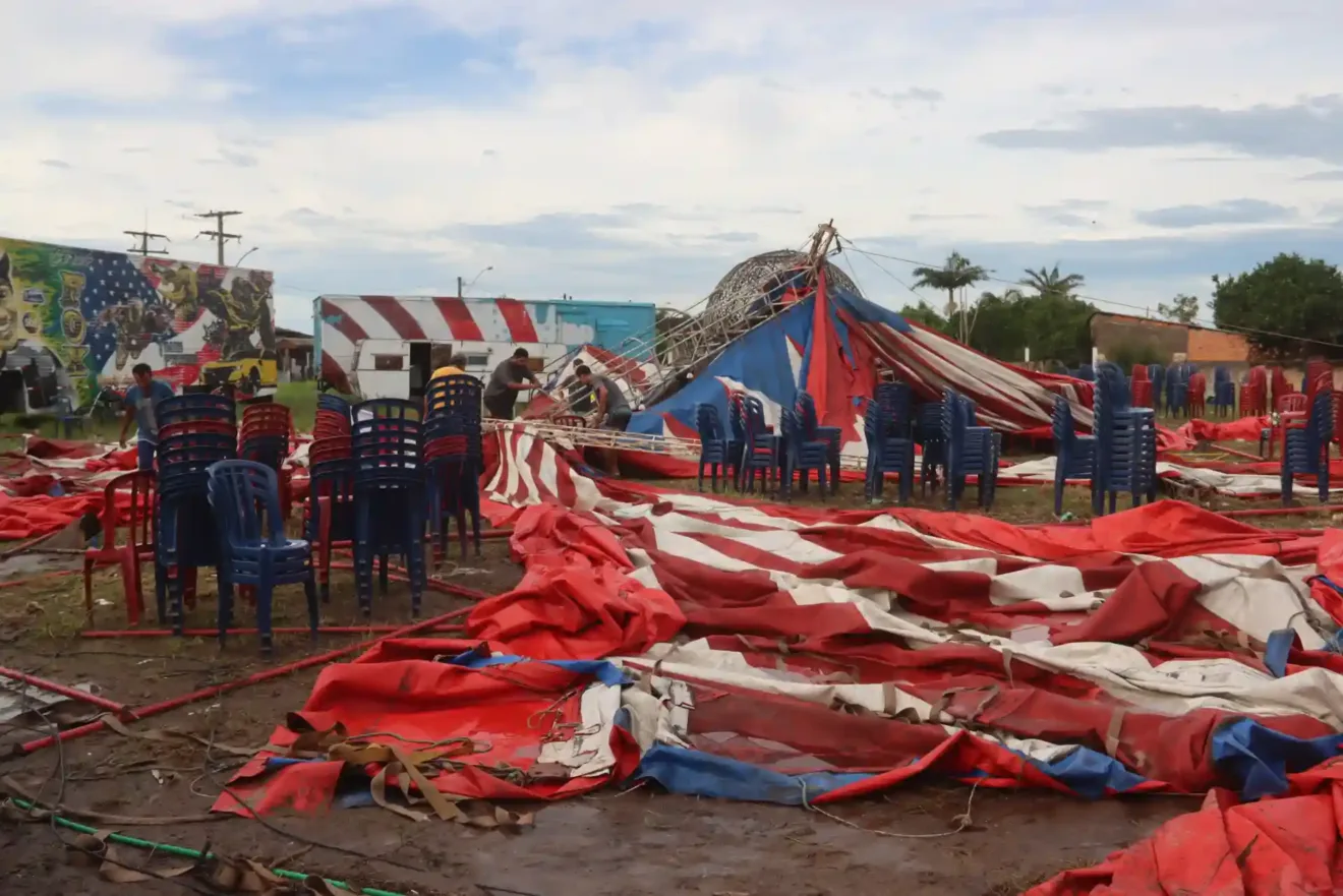 Cenário de circo com lonas danificadas, cadeiras e trabalhadores organizando o espaço. 