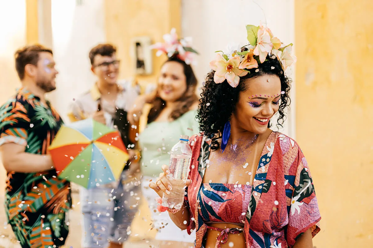 Grupo de amigos se divertindo em uma festa de carnaval com flores na cabeça e confetes no ar