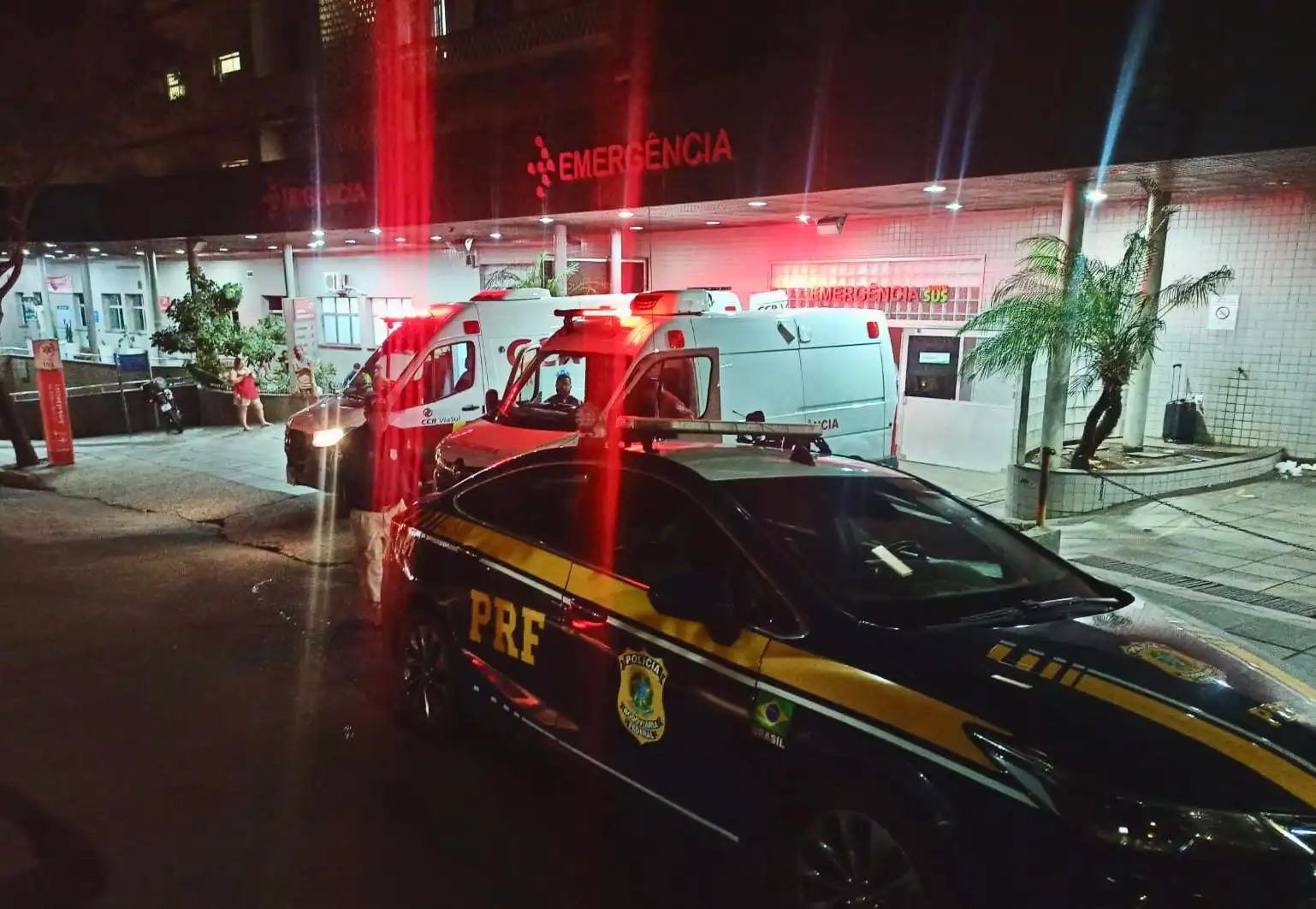 Imagem de veículos de emergência e de polícia na entrada de ao Hospital Cristo Redentor, destacando a sinalização e iluminação noturna.