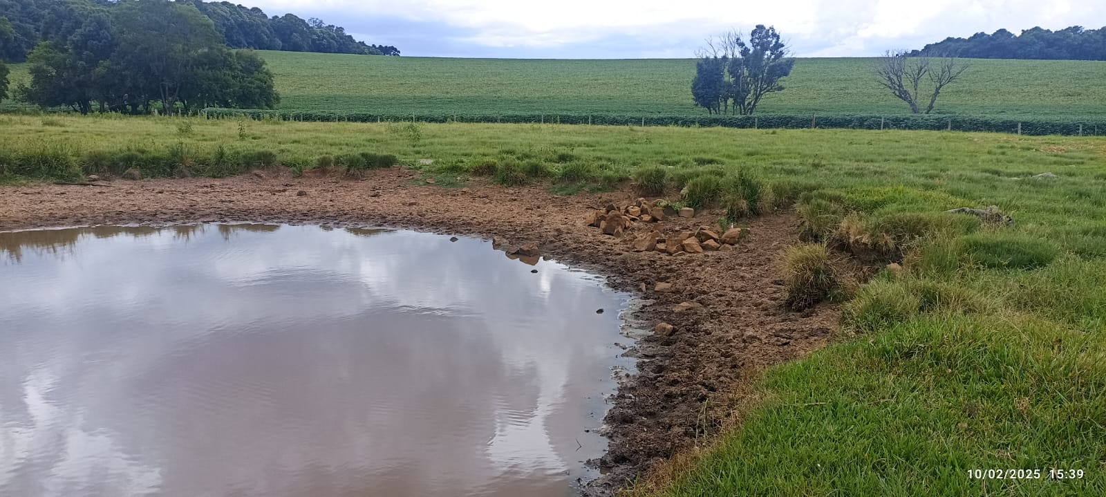 Imagem que retrata a seca em Ernestina, mostrando um açude com nível baixo de água em uma propriedade rural.