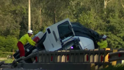 Imagem de um acidente de caminhão, com dois trabalhadores tentando cobrir o veículo com uma lona.