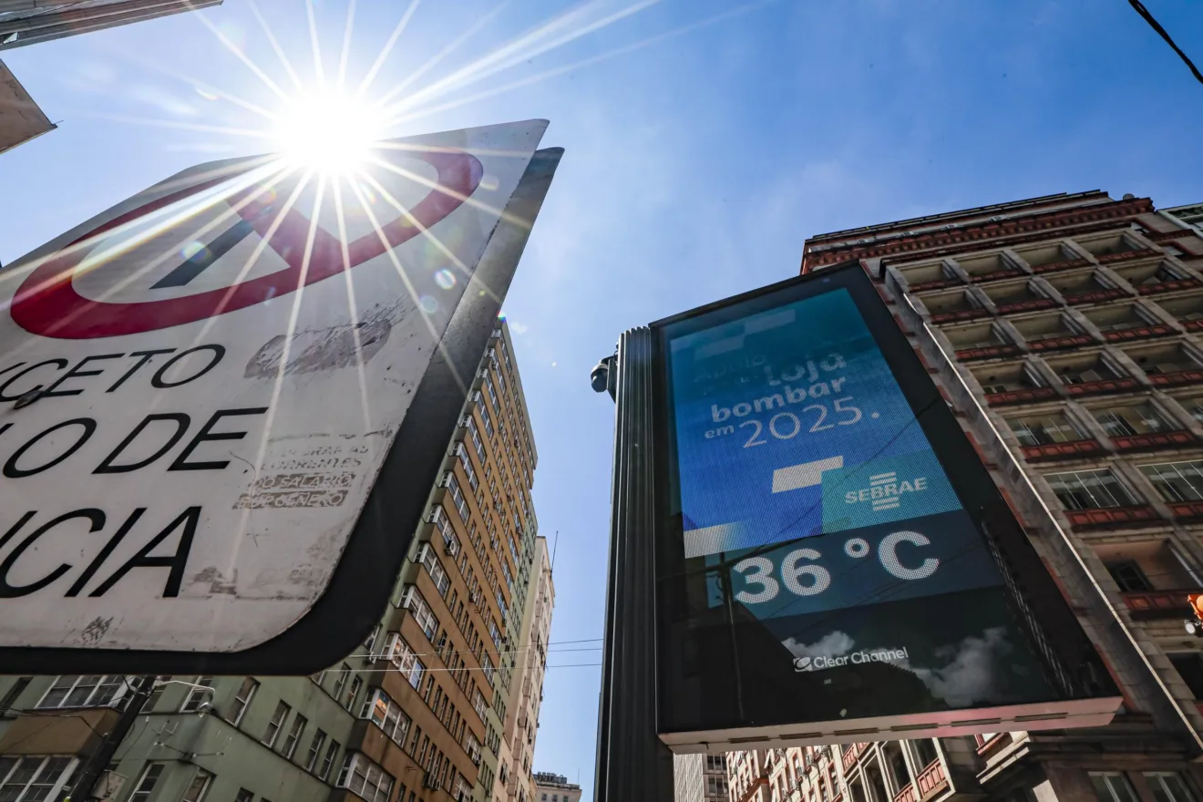 Imagem de um sinal de trânsito e um termômetro de rua mostrando a temperatura de 36°C, sob um céu azul claro no Centro de Porto Alegre.