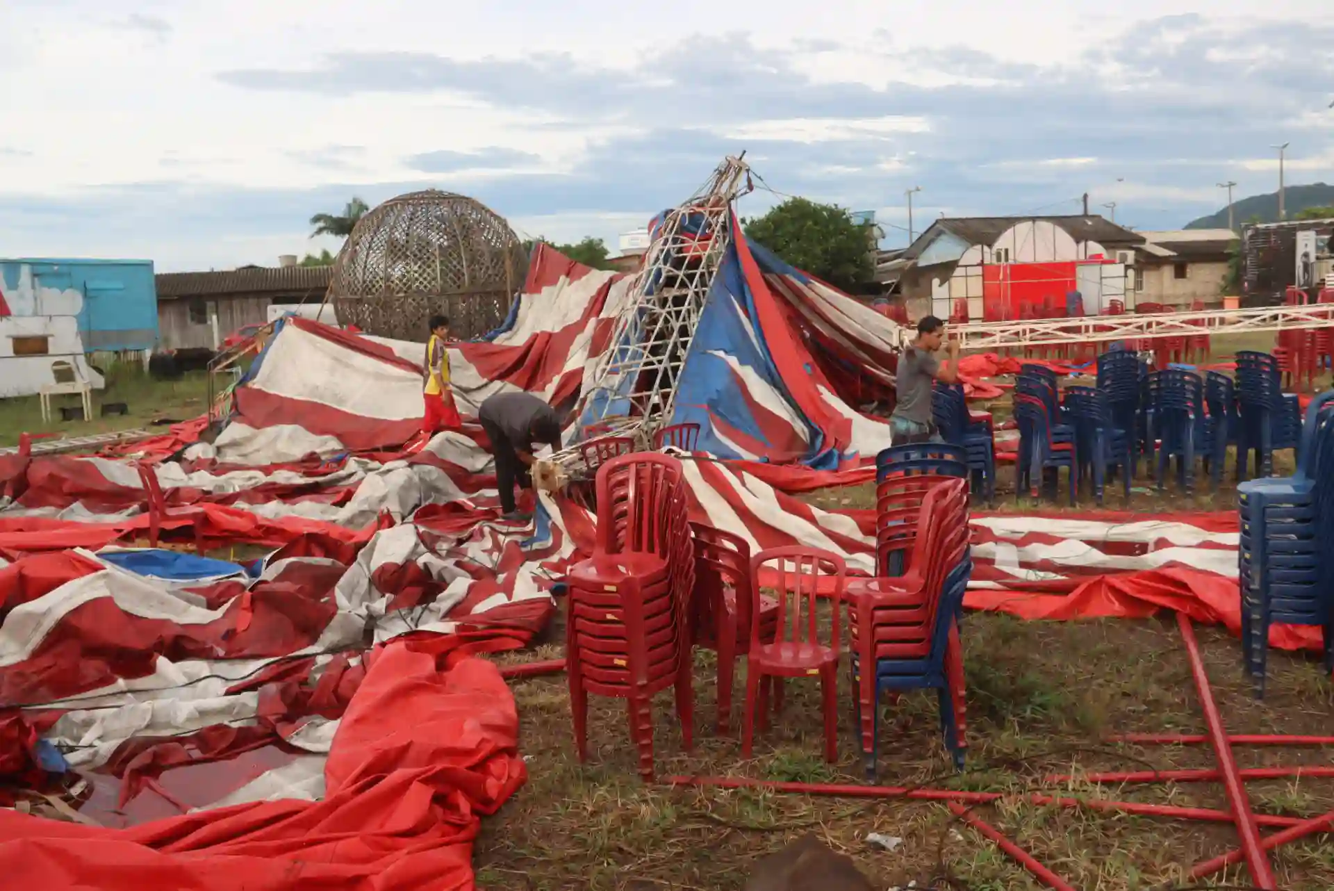 Imagem de um circo após uma tempestade, mostrando tendas rasgadas e cadeiras desordenadas.