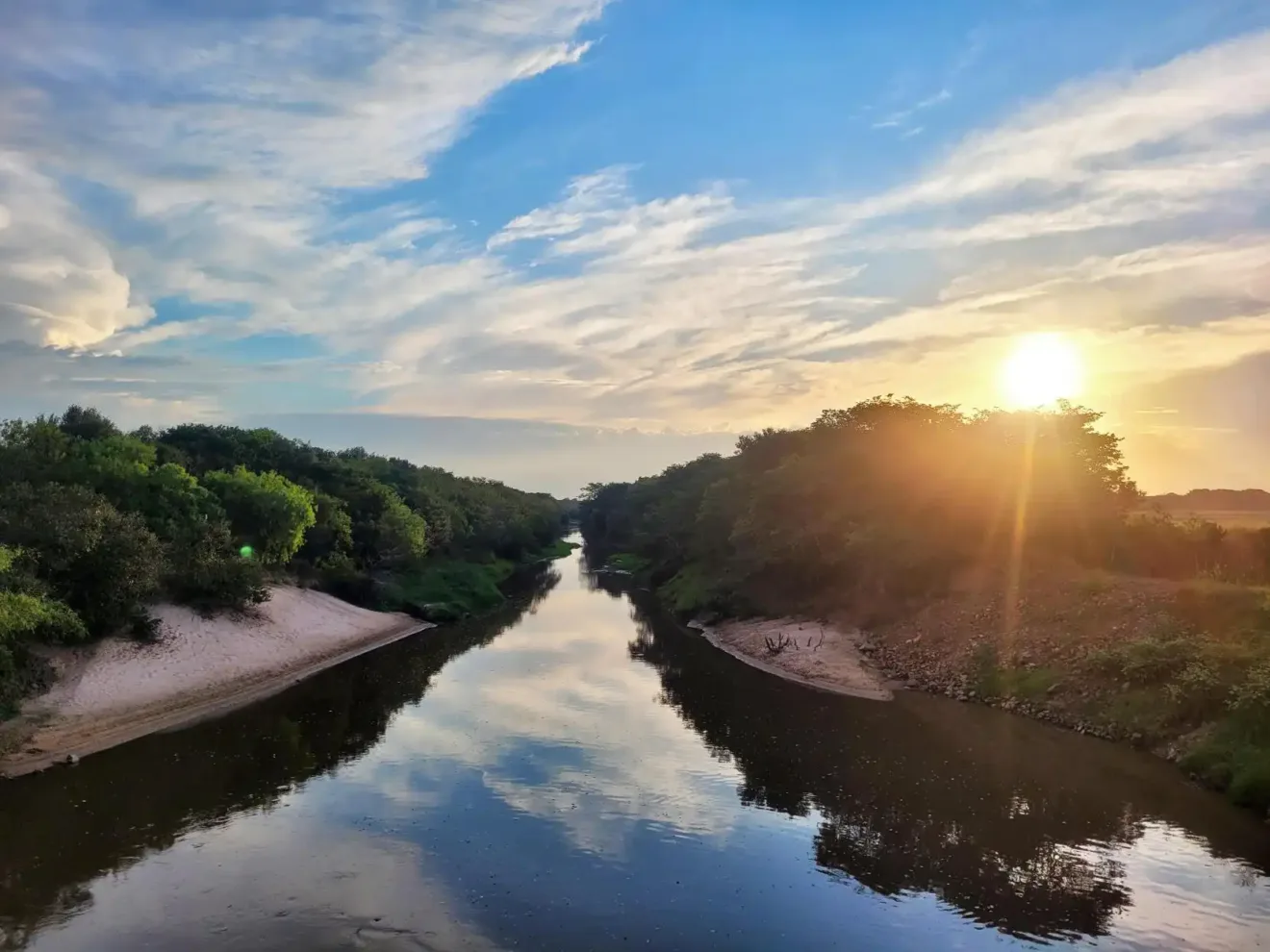 Imagem do Rio Gravataí ao nascer do sol, mostrando suas águas refletindo o céu e a vegetação ao redor, criando um cenário natural espetacular.