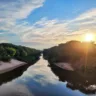 Imagem do Rio Gravataí ao nascer do sol, mostrando suas águas refletindo o céu e a vegetação ao redor, criando um cenário natural espetacular.