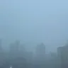 Vista da cidade de Porto Alegre durante uma chuva intensa, com prédios cobertos pela precipitação e baixa visibilidade.