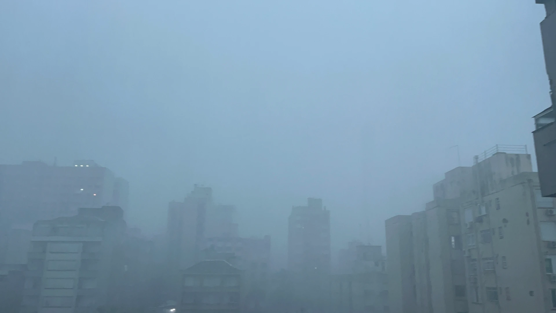 Vista da cidade de Porto Alegre durante uma chuva intensa, com prédios cobertos pela precipitação e baixa visibilidade.