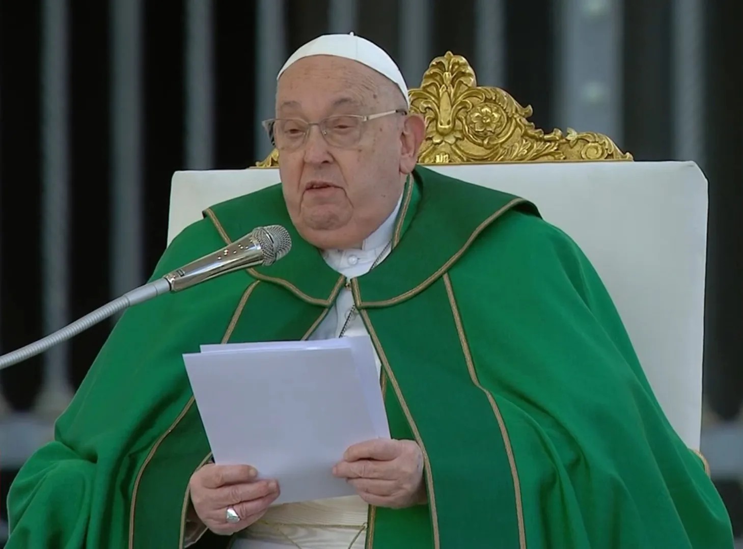 Papa Francisco lendo durante uma cerimônia. Ele usa um manto verde e está em uma cadeira ornada, simbolizando sua posição na Igreja Católica.