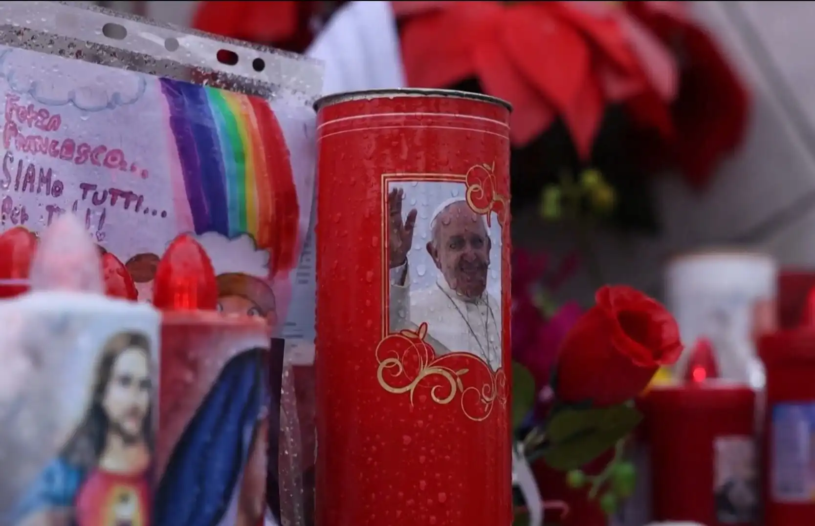 Vela com a imagem do Papa Francisco em um altar decorado com rosas e outros objetos religiosos.