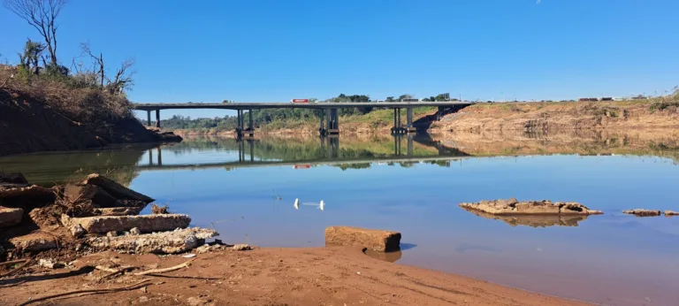 Vista da ponte sobre o rio Taquari, refletindo no espelho d'água sob um céu azul sem nuvens.