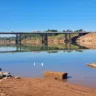 Vista da ponte sobre o rio Taquari, refletindo no espelho d'água sob um céu azul sem nuvens.