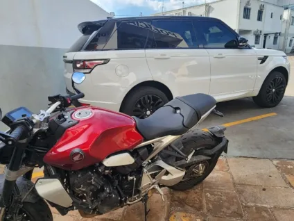 Imagem mostrando uma moto vermelha em primeiro plano e um veículo SUV branco ao fundo, relacionada à Operação Kairós que investiga esquema de pirâmide financeira.