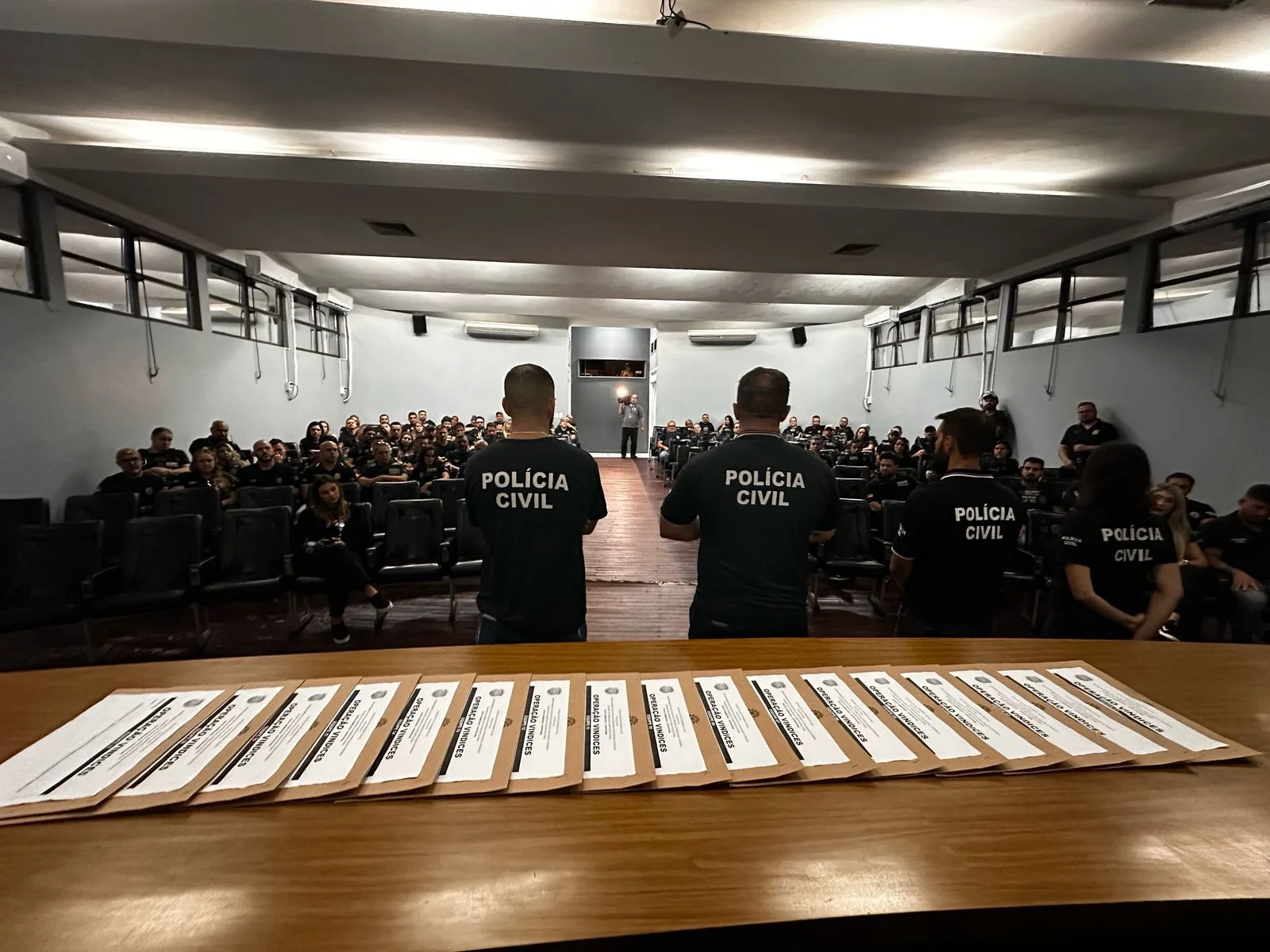 Imagem de uma reunião da Polícia Civil com diversos participantes. Agentes estão em pé em frente a uma plateia lotada