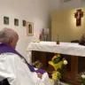 Papa Francisco em momento de oração em um altar, com elementos religiosos ao fundo, incluindo flores, velas e a cruz.