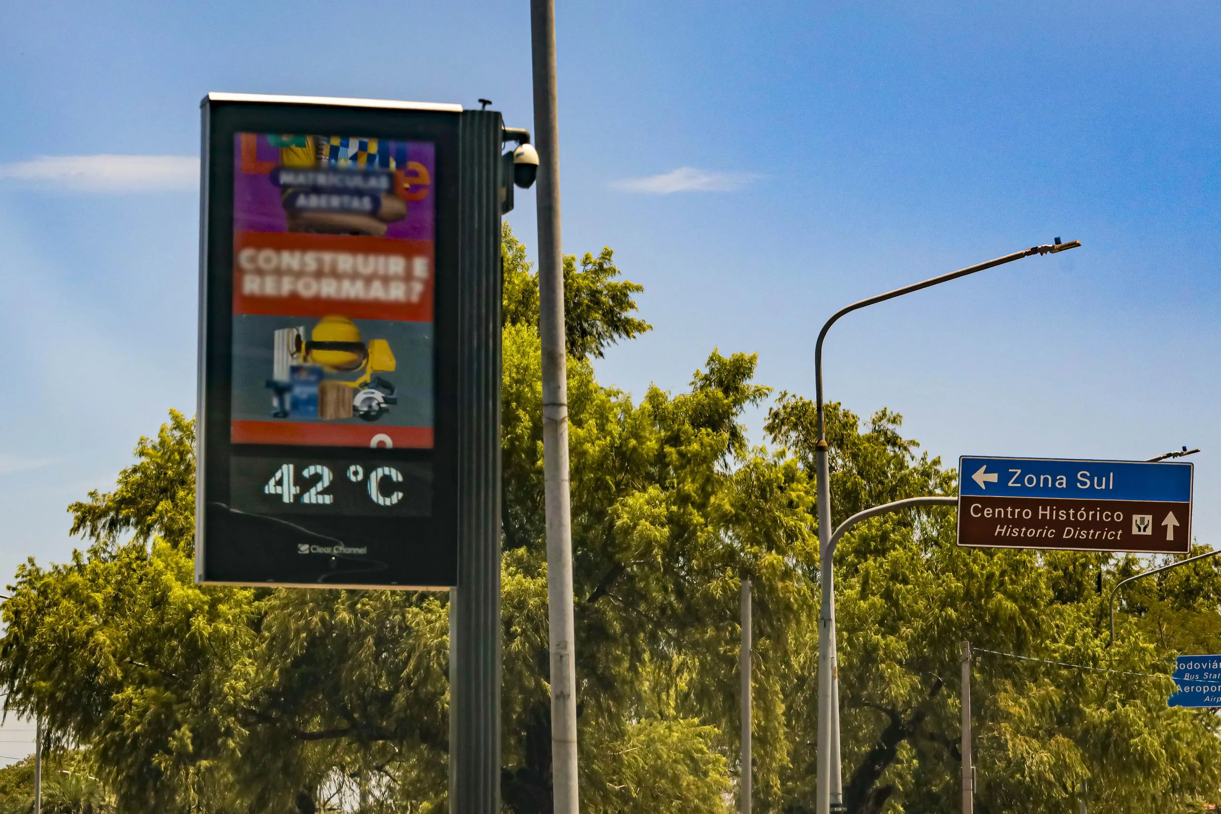 Painel eletrônico com informação de temperatura de 42°C em Porto Alegre, em um dia ensolarado com céu azul.