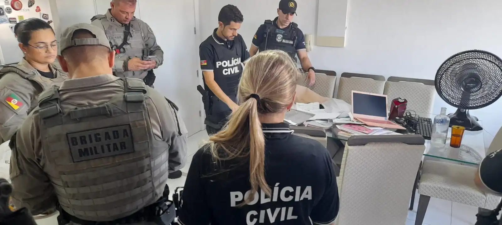 Ação da Polícia Civil em operação contra extorsão e agiotagem, com agentes trabalhando em um ambiente interno.