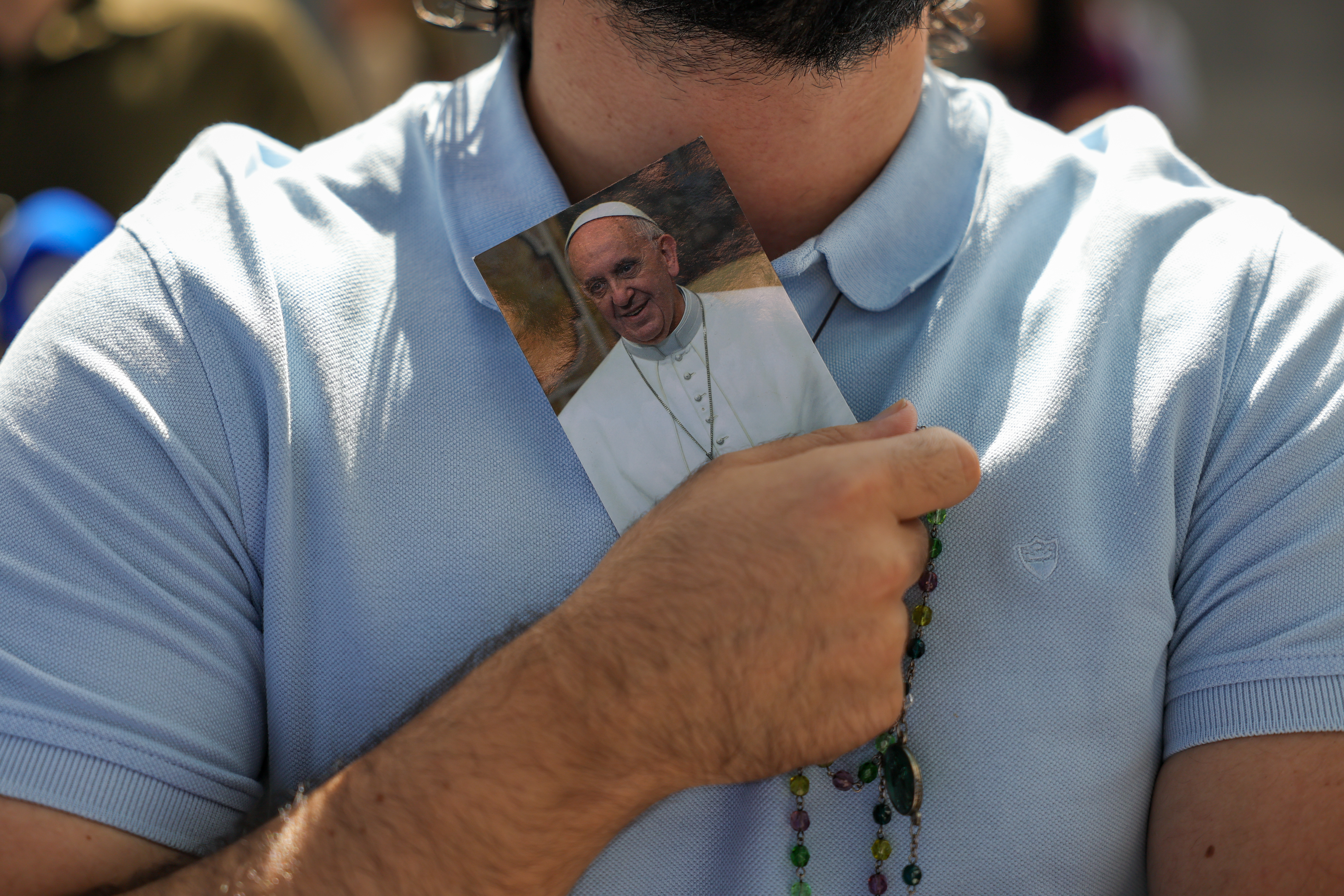 Homem segurando uma imagem do Papa Francisco e um rosário.