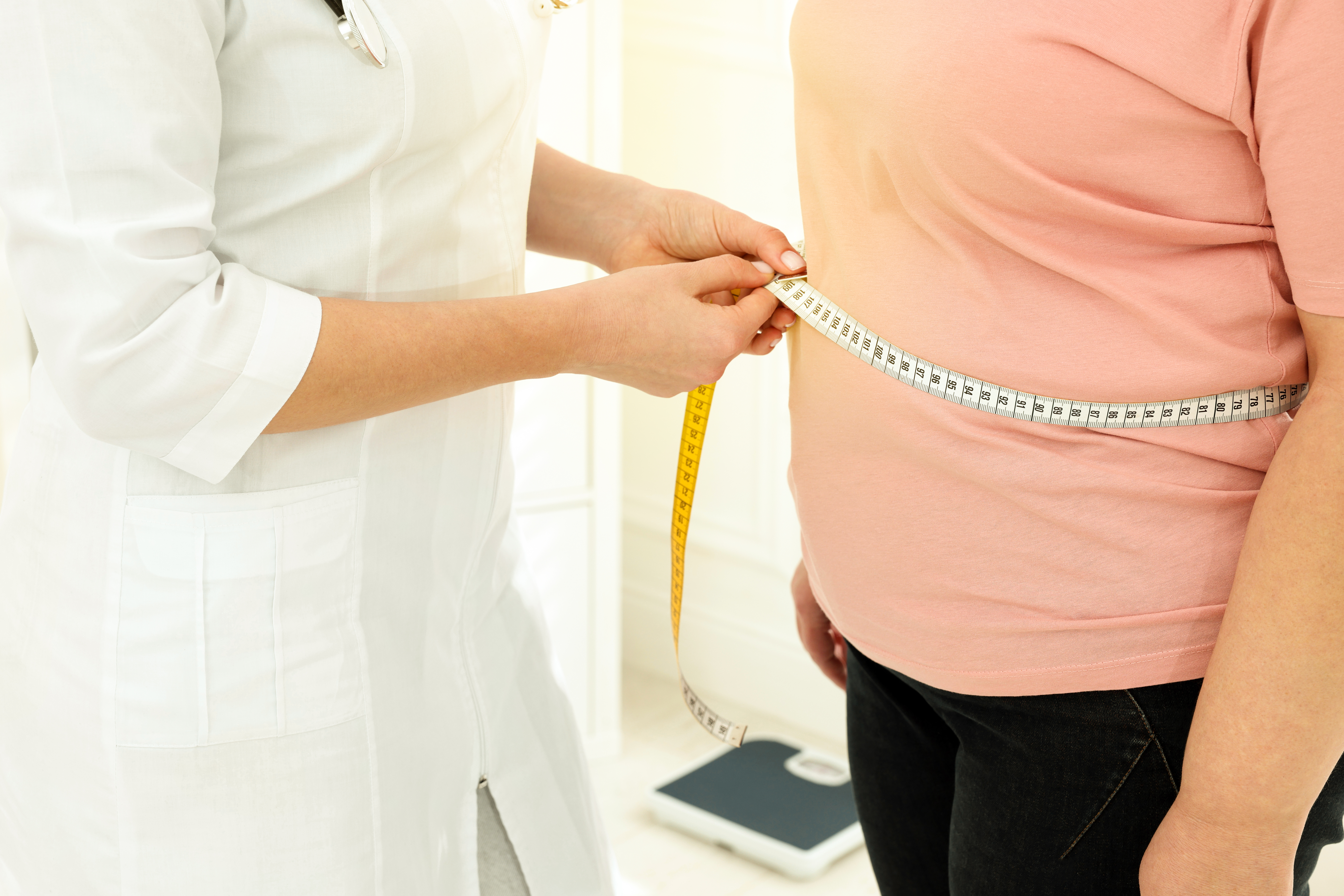 Nutricionista medindo a cintura de uma mulher com fita métrica em uma clínica.