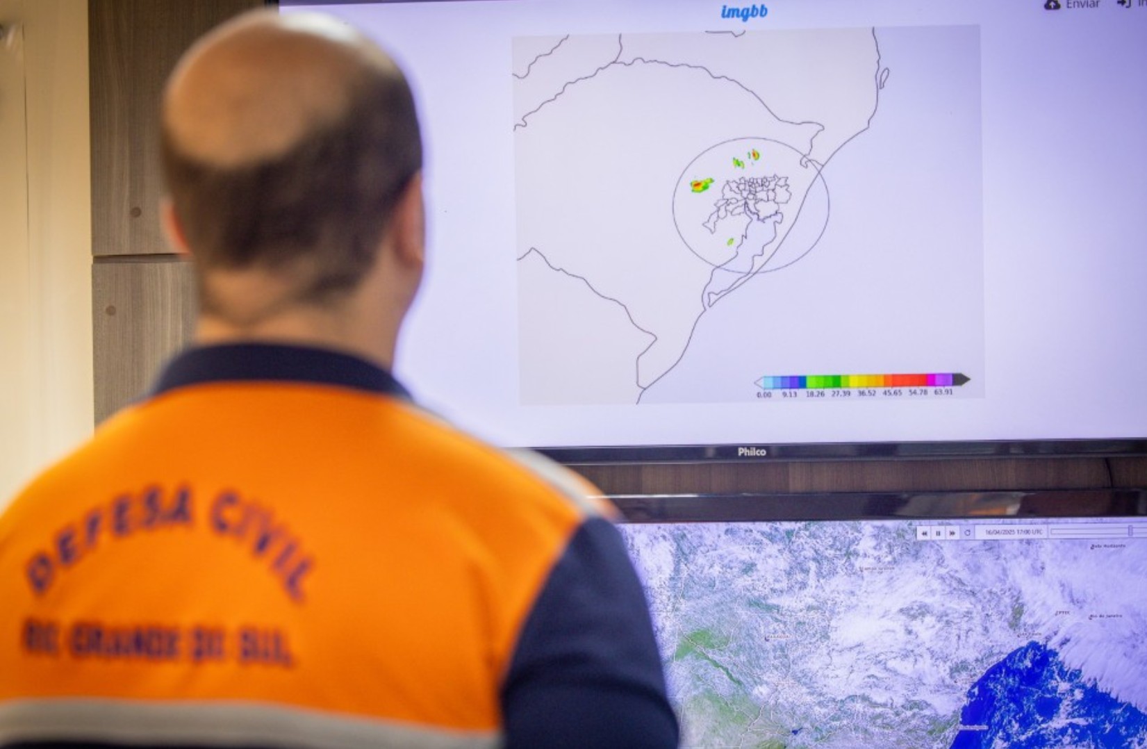 Funcionário da Defesa Civil do Rio Grande do Sul observando um monitor com dados meteorológicos.