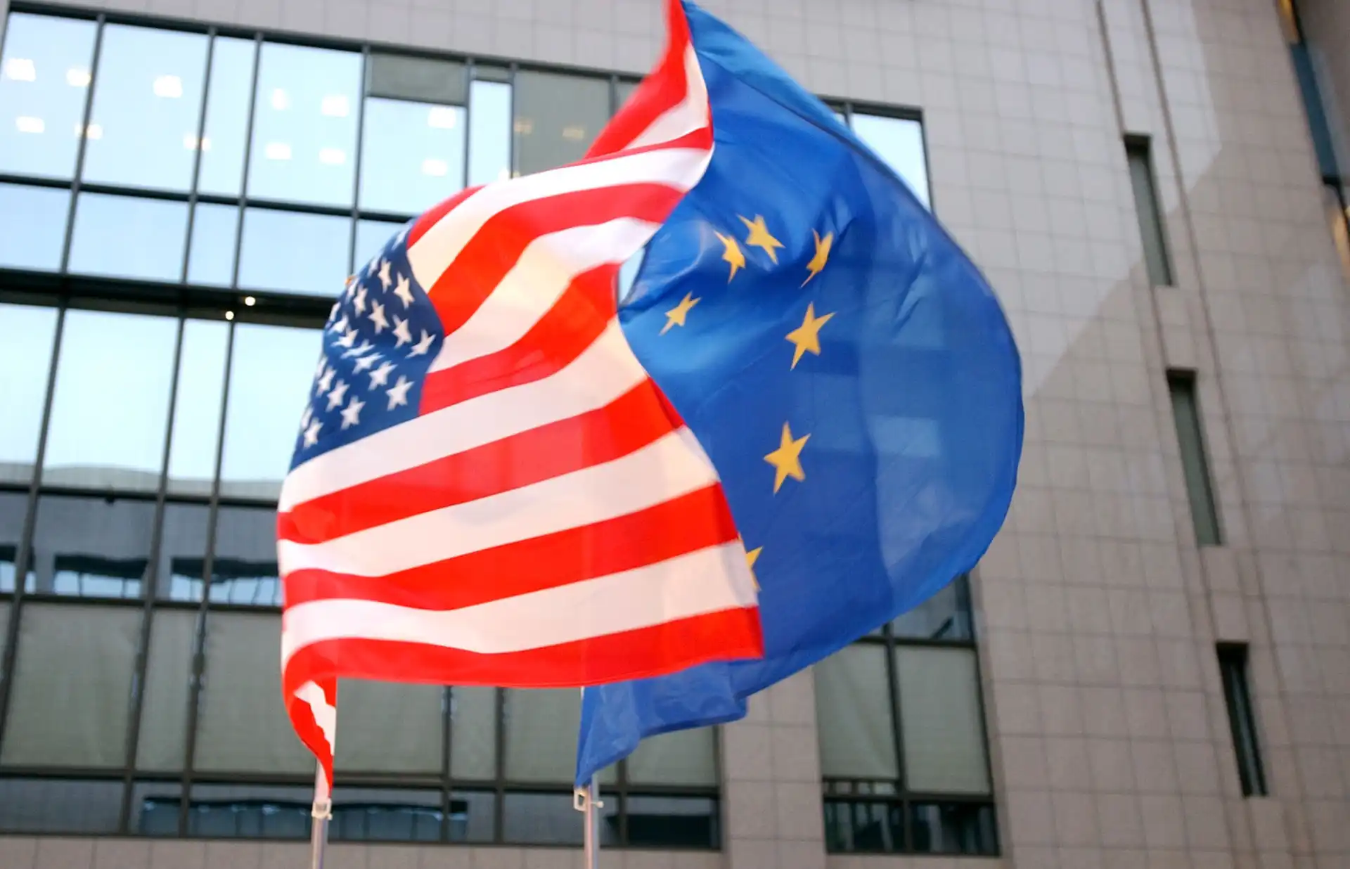 Bandeiras dos Estados Unidos e da União Europeia tremulando juntas.