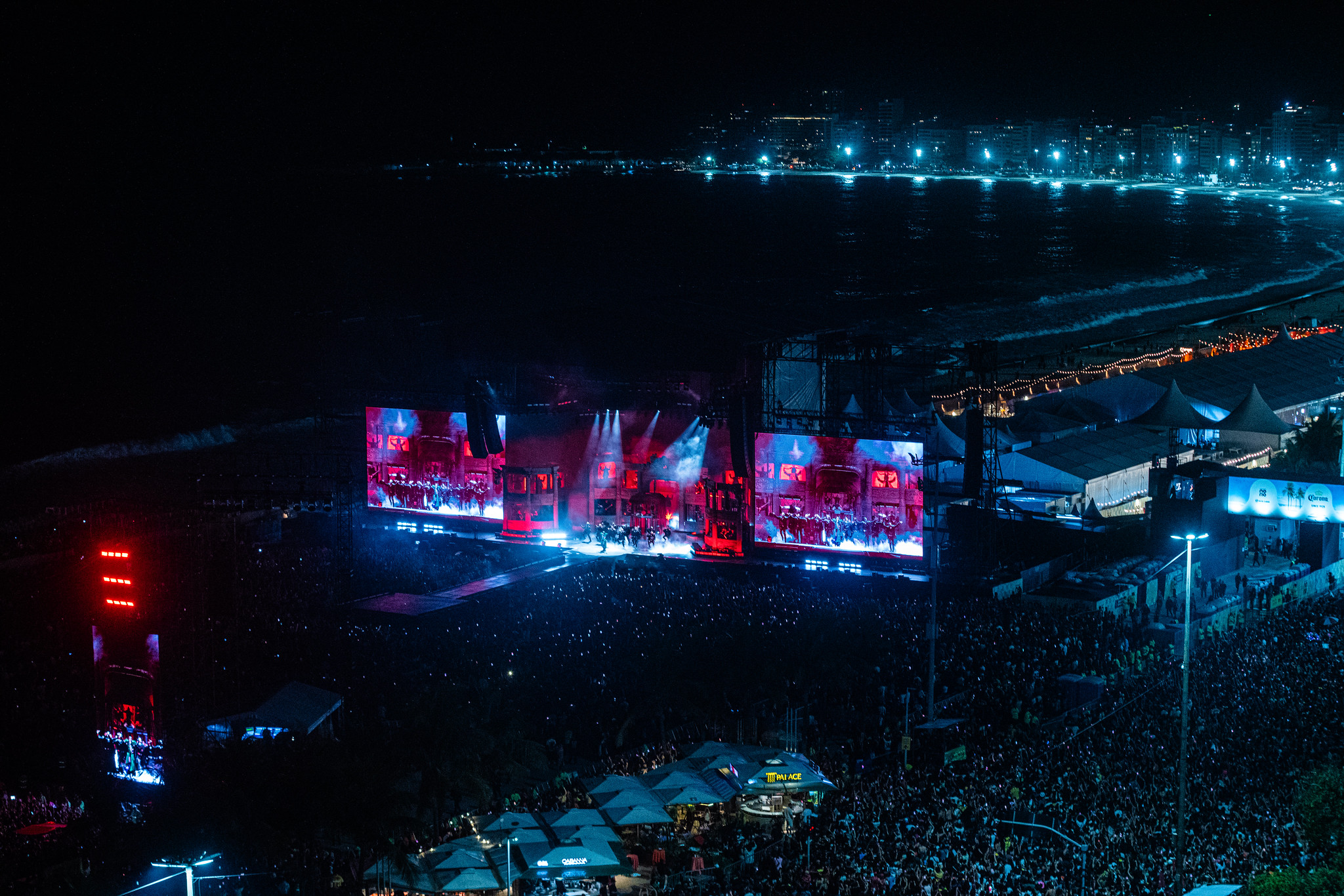Foto panorâmica do palco do Show da Lady Gaga em Copacabana. É noite e há luzes coloridas e milhares de pessoas