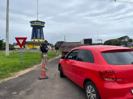 Agente da PRF fiscaliza carro vermelho durante operação do feriado do Dia do Trabalhador