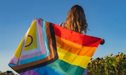 Mulher jovem de costas com uma bandeira da Luta LGBTQIAPN+