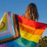 Mulher jovem de costas com uma bandeira da Luta LGBTQIAPN+