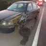 Um carro de cor escura com marca de acidente em meio a uma rodovia