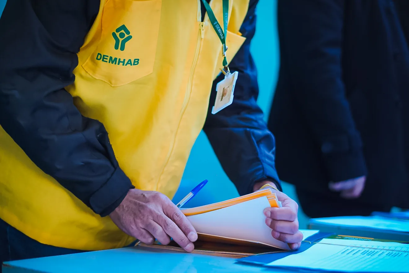 Profissional do DEMHAB organizando documentos em mesa de trabalho.