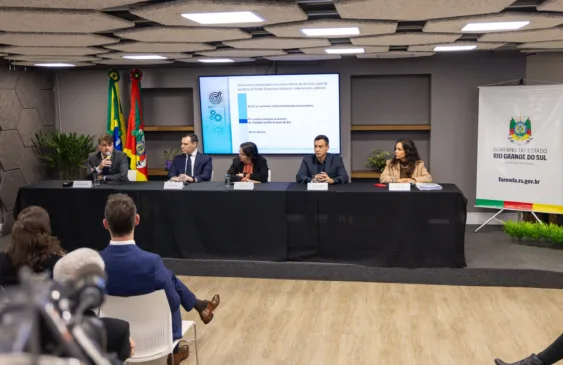 Foto da mesa com cinco pessoas concedendo entrevista coletiva sobre descontos em folha de pagamento de servidores inativos. Duas pessoas da plateia podem ser vistas de costas.