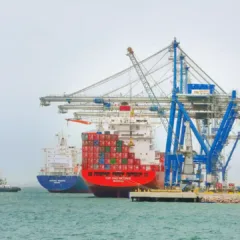 Imagem do Porto de Rio Grande, com uma grande embarcação de carga e contêineres sendo carregada por guindastes.