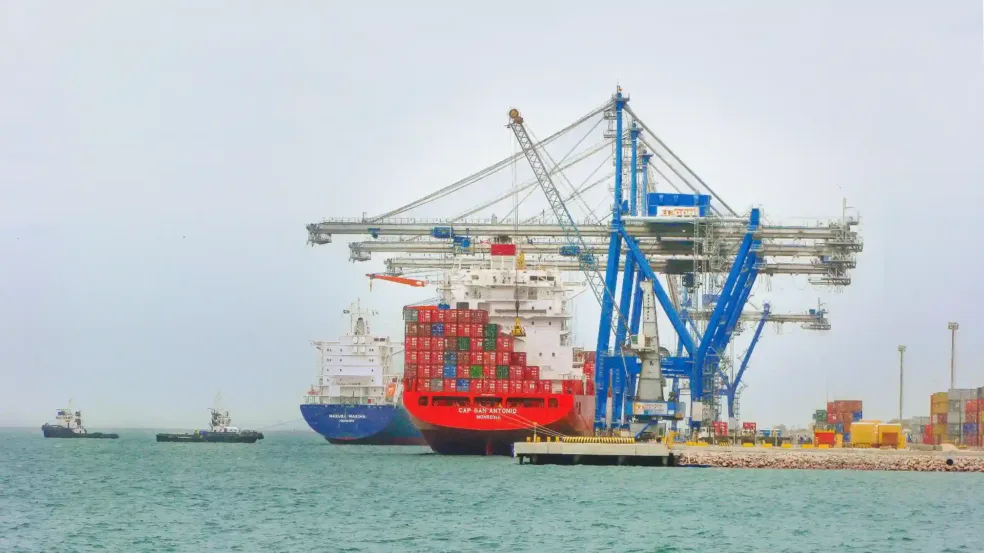 Imagem do Porto de Rio Grande, com uma grande embarcação de carga e contêineres sendo carregada por guindastes.