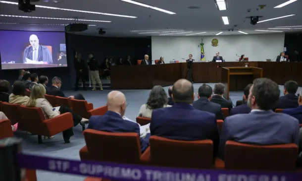 Auditório do STF, foto tirada das cadeiras, enquadrando pessoas de costas, com a imagem de Alexandre de Moraes no telão